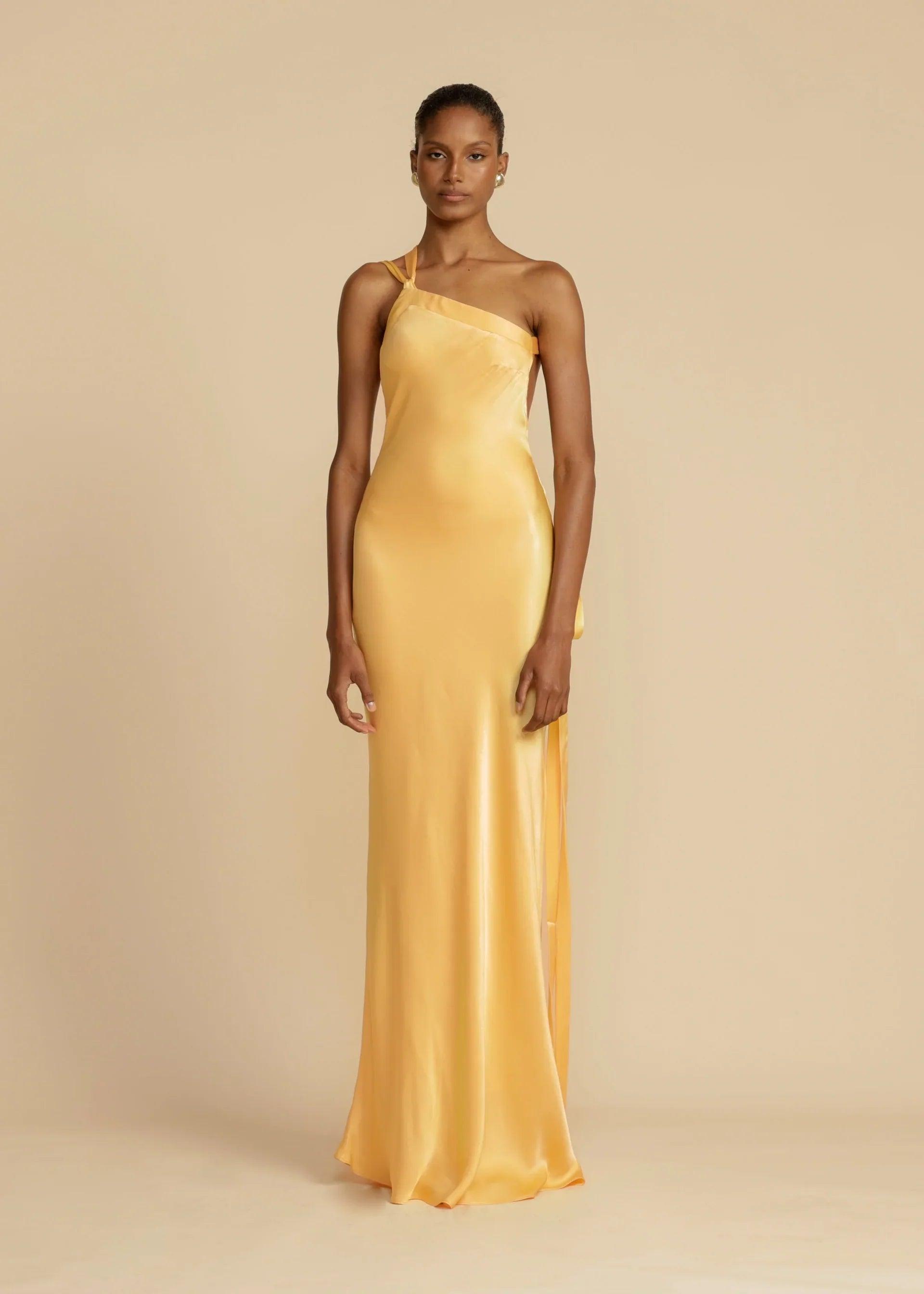 Vestido Longo Aurelia em satin jacquard amarelo com decote assimétrico e costas abertas, ideal para eventos sofisticados. Majestique.