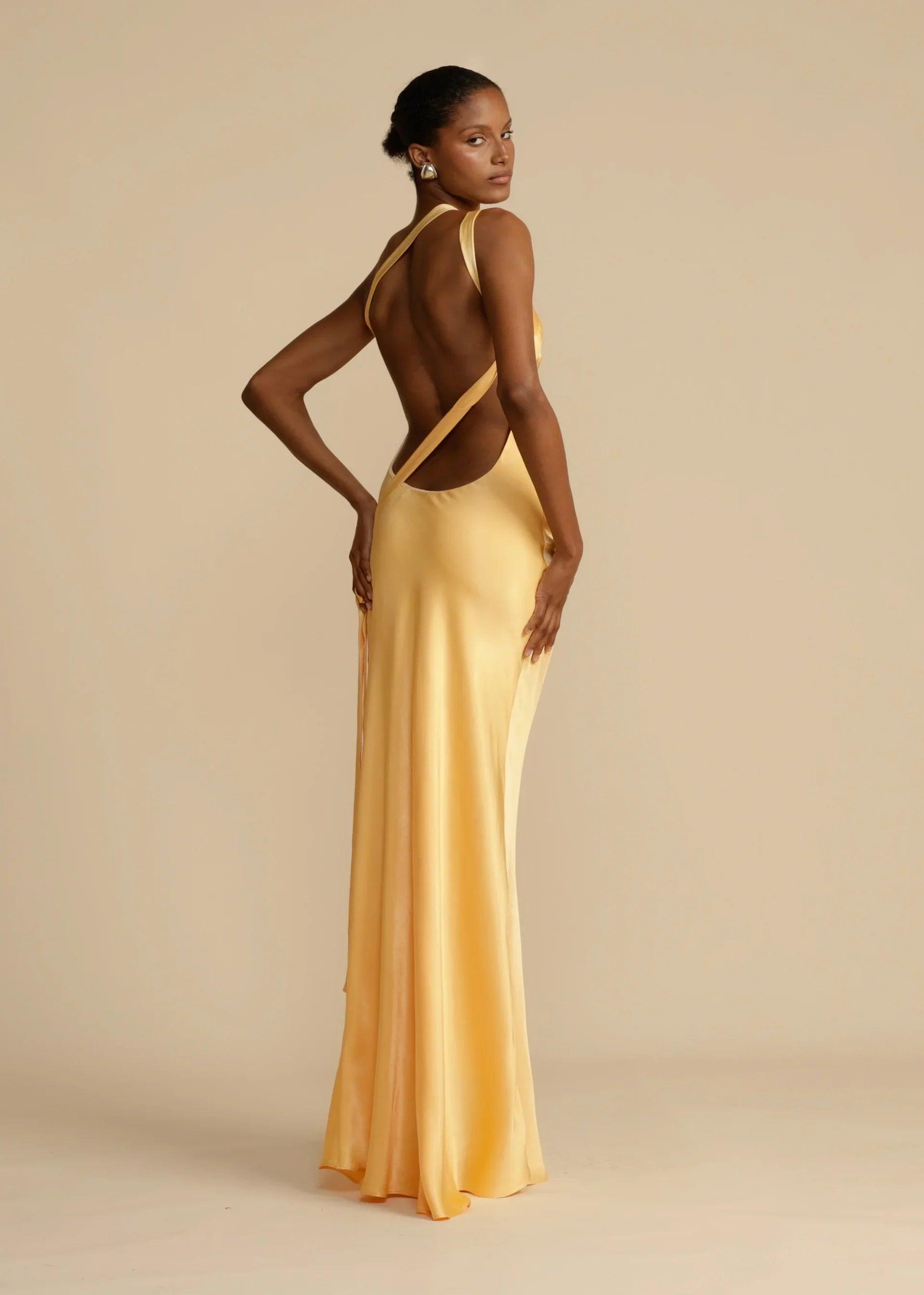 Vestido Longo Aurelia em satin jacquard amarelo com decote assimétrico e costas abertas, ideal para eventos sofisticados. Majestique.1