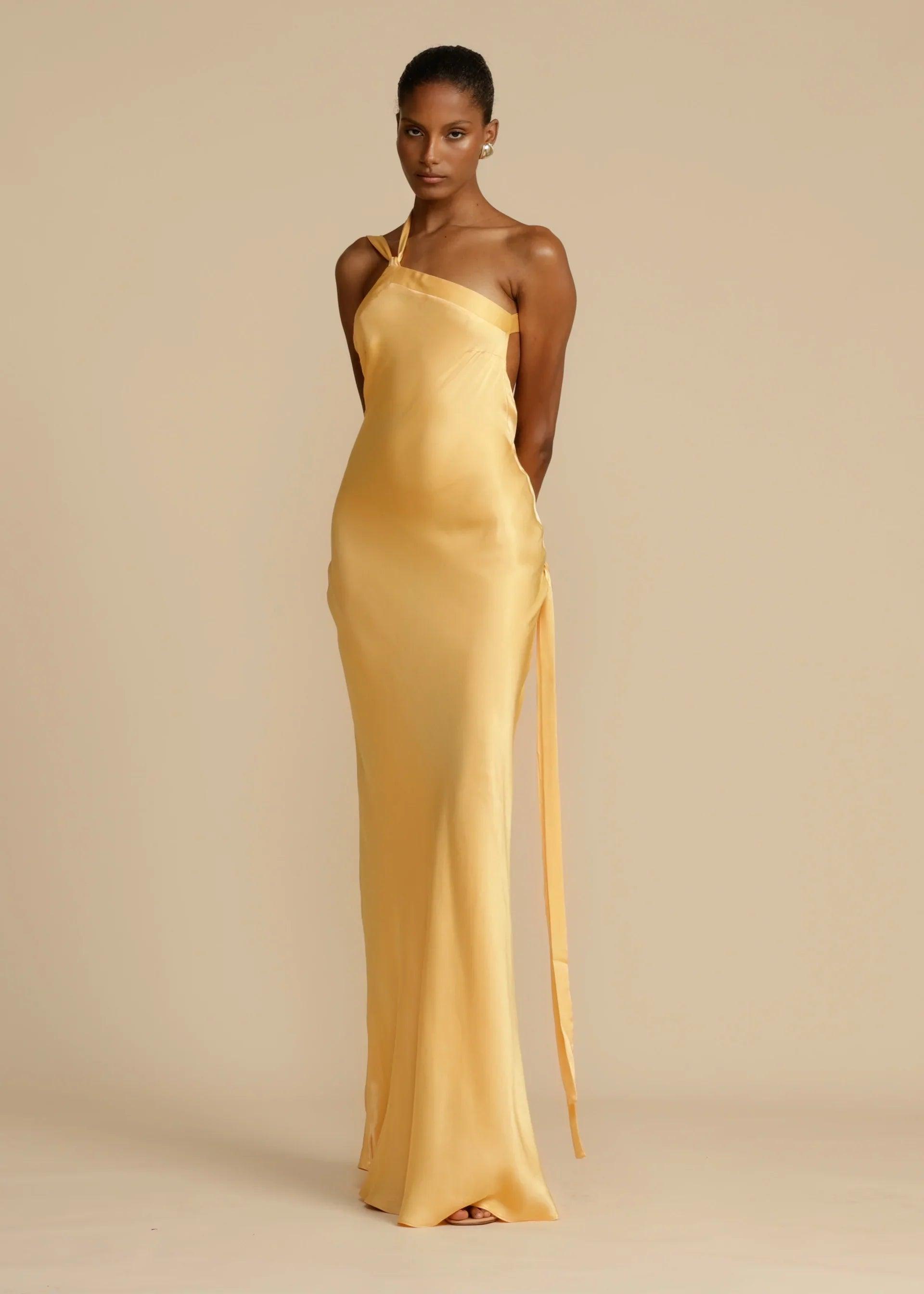 Vestido Longo Aurelia em satin jacquard amarelo com decote assimétrico e costas abertas, ideal para eventos sofisticados. Majestique.2