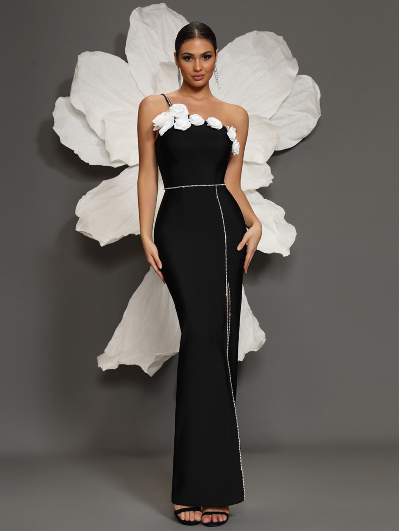 Vestido longo preto com alça assimétrica, flores brancas aplicadas e fenda com detalhe em cristais
